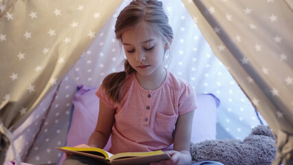 Preteen kid reading book in wigwam with lighting at home. © LIGHTFIELD STUDIOS
