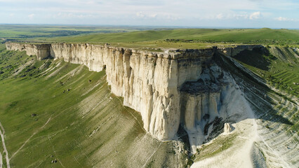 Wonderful white cliff in Crimea in a sunny summer day. Shot. Aerial for unusual shaped mountain and green field with trees.