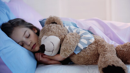 Child in pajama sleeping with soft toy at home.