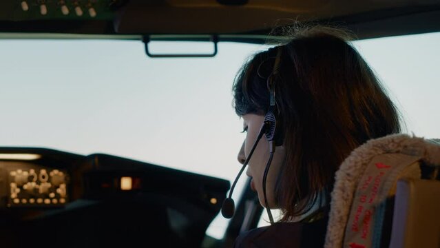 Woman copilot in uniform preparing to takeoff for airline flight, pushing buttons on dashboard and control panel command in cockpit. Flying airplane with aerial navigation and radar. Close up.