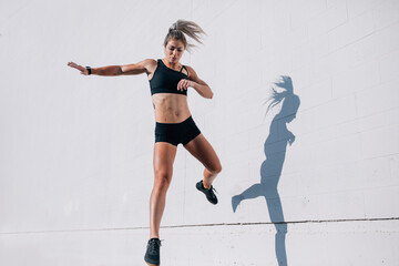 Fitness woman wearing black running and jumping in air against w