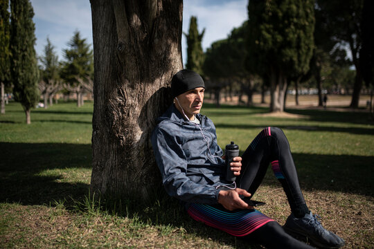 Man relaxing in park, he is sitting on grass leaning on a tree. - Powered by Adobe