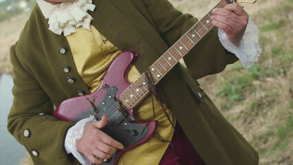 Close up for man with a purple electric guitar playing in old fashioned costume of rococo manner on...