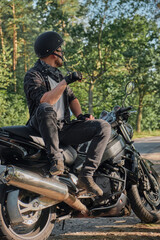 Fototapeta premium Young male biker in helmet travels on a motorcycle alone, stopped and smoking on the side of a forest road