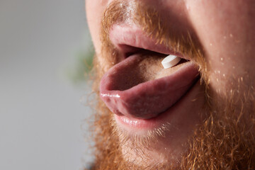 Man taking pill, mouth open with tongue sticking out.