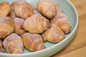 Homemade baked croissants bagels on plate on wooden table closeup macro, bagels with white sugar powder