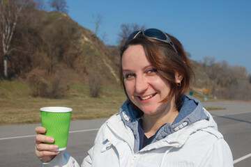 Woman holds the green glass. The young woman drinks coffee in the street