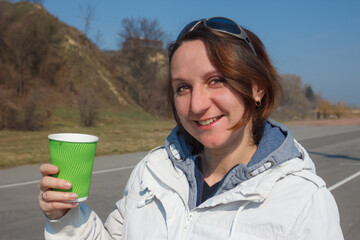 Woman holds the green glass. The young woman drinks coffee in the street