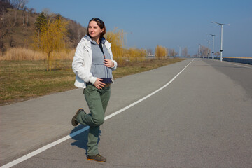 Pregnant woman in the white jacket walks in sunny weather