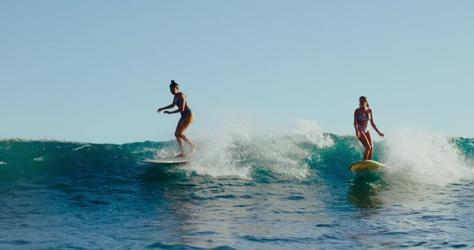 Beautiful stylish girls riding wave at sunset in Hawaii, summer lifestyle longboarding, best friends surfing together, summer lifestyle