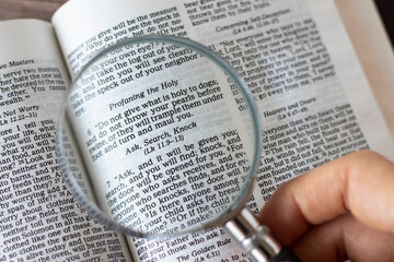 Ask, search, knock, biblical text verse. Human hand holding a magnifying glass over Holy Bible...