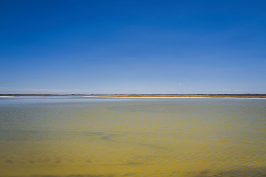 Tranquil minimalistic landscape of the blue sky, horizon, and warm glowing water of Chaplin Lake, the salt lake, in Canada