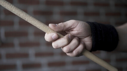 Close up of man hand with black fabric bracelet on his wrist holding drumstick and rotating it with the help of his fingers on a red brick wall background. Action. Musical instruments concept.