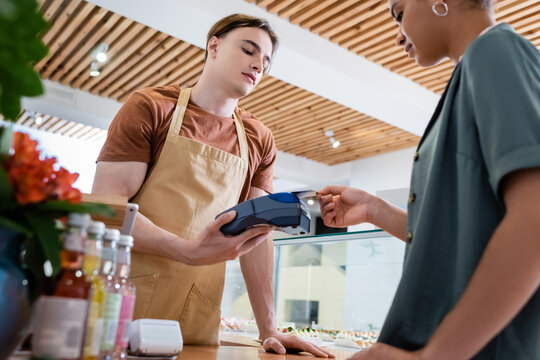 Low angle view of african american customer paying with credit card near seller in confectionery.