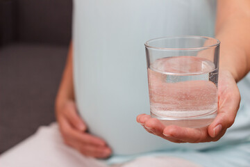Pregnant drinks mineral water. The pregnant woman holds a glass of mineral water.