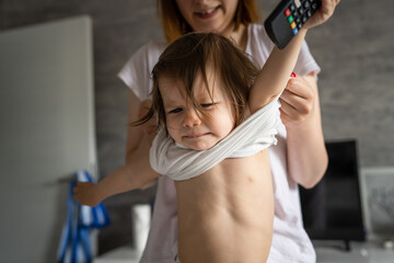 One small caucasian girl toddler standing on the bed at home protesting while her mother is changing her clothes real people growing up copy space
