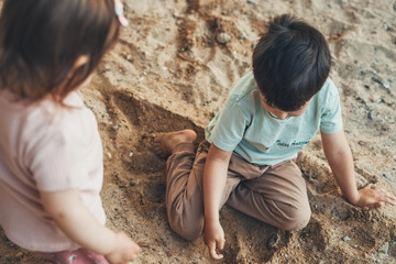 Older brother and his baby sister sitting on the sand in the home garden, playing with the sand. Healthy lifestyle. Home garden.