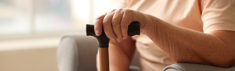 Elderly woman with walking stick at home, closeup