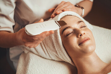 Beautiful ginger woman receiving ultrasonic facial exfoliation at spa salon. Skin care. Medical...