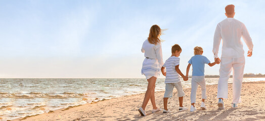 Young family walking on sea beach, back view