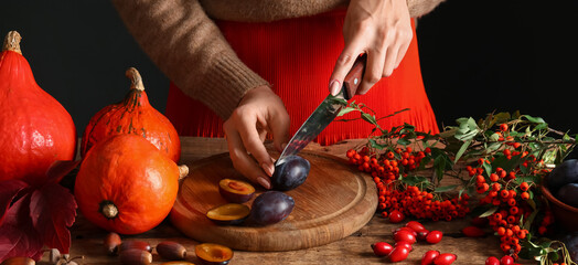 Woman cutting fresh plums at wooden table against dark background