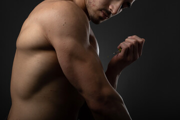 Muscular man with a syringe in his hand. User of anabolic steroids for strength training.