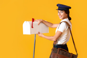 Young postwoman with mailbox on yellow background