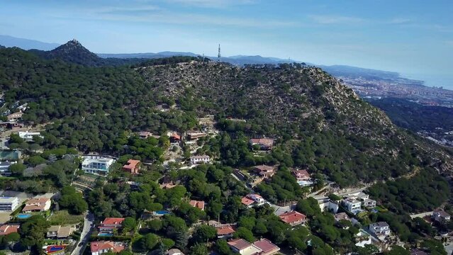 fly by drone panoramic travelling of an urbanization on the Catalan Costa Brava in Barcelona  surrounded by detached houses, nature the mountains during a summer afternoon on a sunny day  blue skies