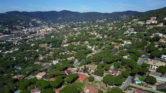 fly by shot of an urbanization on the Catalan Costa Brava in Barcelona  surrounded by detached houses, nature and the mountain during a summer afternoon on a sunny day