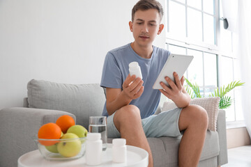 Young man with pill bottle and tablet computer at home