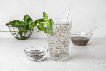 Glass with water and chia seeds on light background