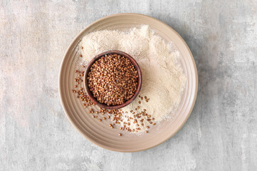 Plate with bowl of buckwheat grains and flour on grunge background