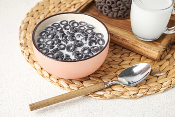 Bowl of tasty cereal rings with milk and spoon on light background