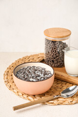Bowl of tasty cereal rings with milk and spoon on light background