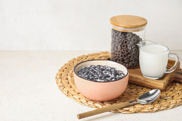 Bowl of tasty cereal rings with milk and spoon on light background