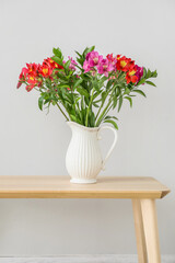 Vase with bouquet of beautiful alstroemeria flowers on wooden table near light wall