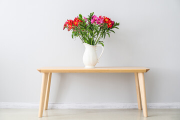 Vase with beautiful alstroemeria flowers on wooden table near light wall