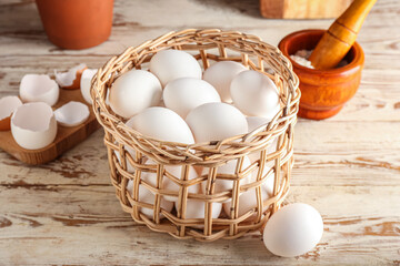 Wicker basket with eggs on light wooden table