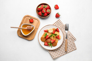 Plate with mini pancakes, delicious strawberry and honey on light background