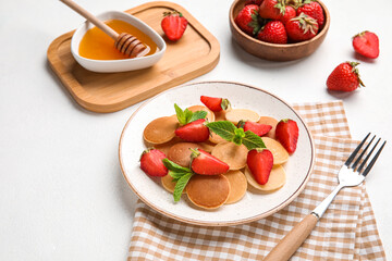 Plate with mini pancakes and delicious strawberry on light table