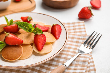 Plate with mini pancakes and delicious strawberry on light table, closeup