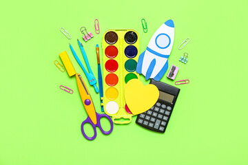 Paper rocket with school stationery on green background