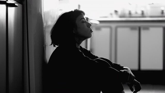 Person suffering from mental illness sitting on floor at home in monochrome. Girl struggling with depression in black and white photography