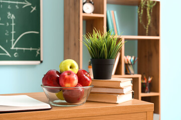 Bowl with apples, books and flowerpot on table in classroom