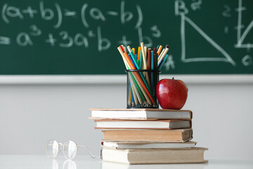 Red apple with school books, pen cup and eyeglasses on table in classroom