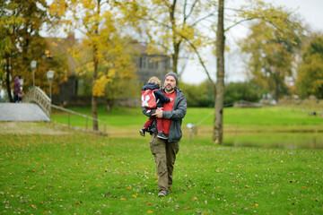 Cute toddler boy in his fathers arms. Dad and son having fun on sunny autumn day. Adorable son being held by his daddy.