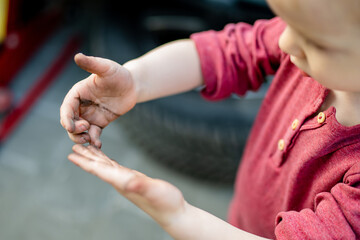 Funny toddler boy showing his dirty little hands. Child getting dirty while playing in the backyard.