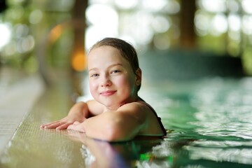 Cute young girl having fun in indoor pool. Child learning to swim. Kid having fun with water toys. Family fun in a pool.