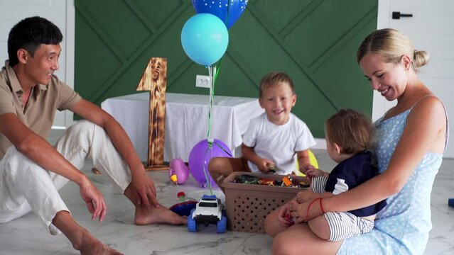 A korean father and caucasian mother are playing with their sons on the floor at home. It's the firts birthday of the youngest son. Happy family and adorable metis kids