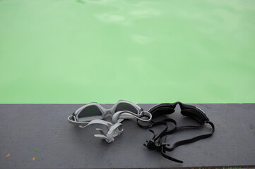 Two waterproof goggles, they are placed on the edge of the pool.	